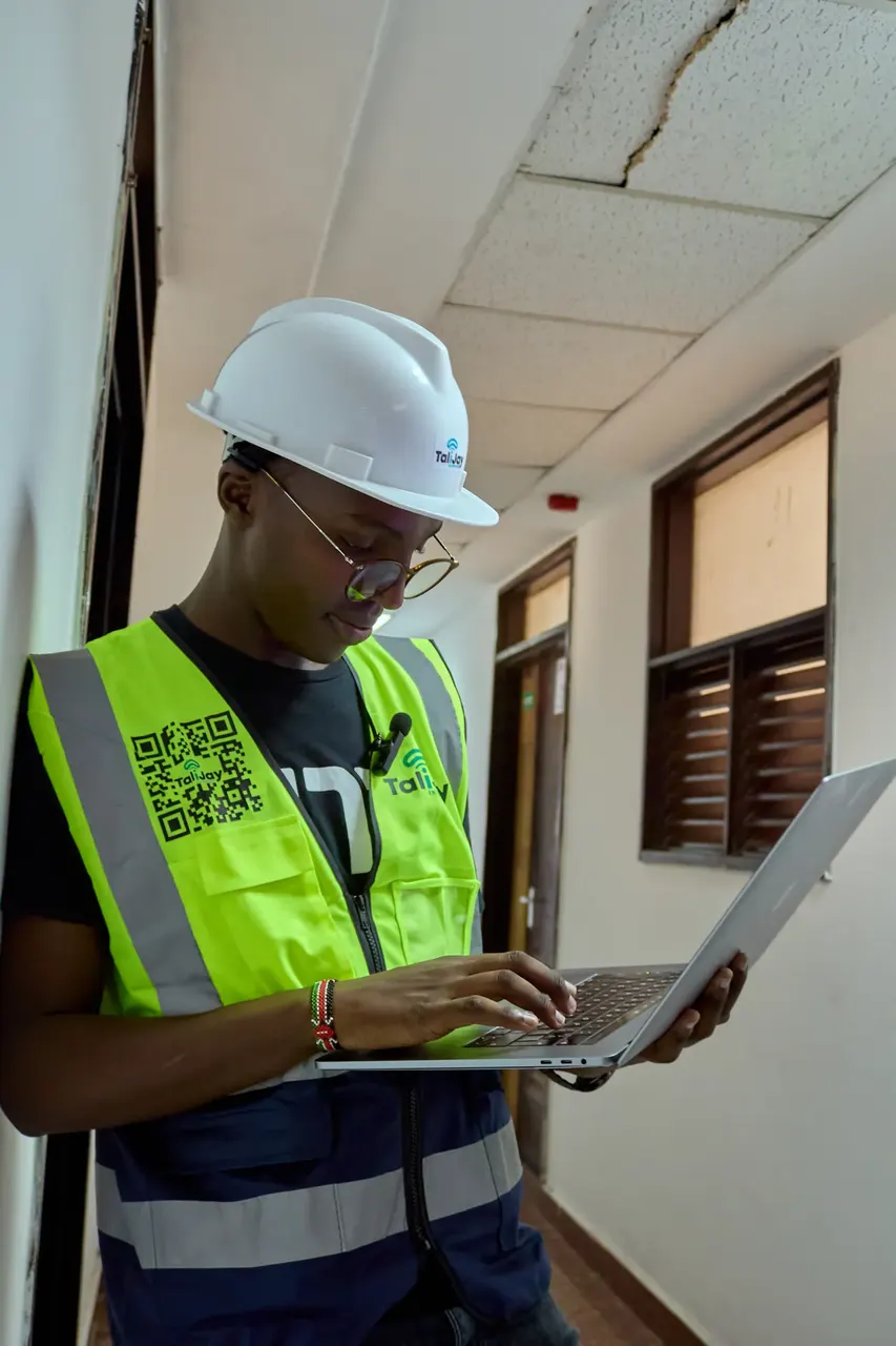 Engineer in a hard hat and high-visibility vest working on a laptop on site